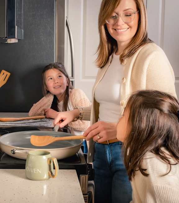 A woman and two young girls are in a kitchen, with the woman standing and the girls sitting at a counter.