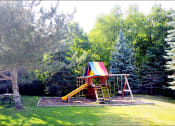 Thumbnail 16 of 23 - outdoor playground with slide and swing next to a park bench and large trees all around