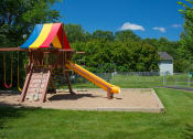 Thumbnail 19 of 22 - children's outdoor playground with swings, climbing wall, slide, and rainbow canopy, on a sunny day