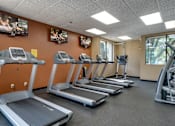 Thumbnail 11 of 17 - Fitness room with treadmills facing TVs on an orange wall