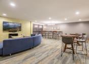 Thumbnail 16 of 27 - Lounge with tables and chairs, and a blue circular couch facing a wall-mounted TV