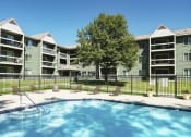 Thumbnail 16 of 19 - Outdoor pool with lounge chairs, surrounded by a black fence with the apartment building in the background