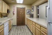 Thumbnail 8 of 17 - Community kitchen with light wooden cupboards and a galley layout. A stove, oven, and microwave on the left, a refrigerator on the right