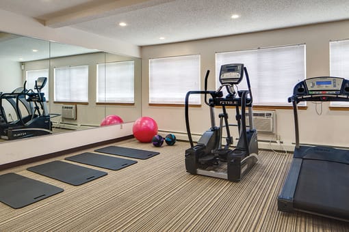 Fitness center with a treadmill, elliptical, yoga mats, and large mirrors