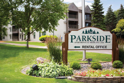 Sign that says "Parkside apartments at Medicine Lake" on it with the words "Rental Office" and a left arrow below it