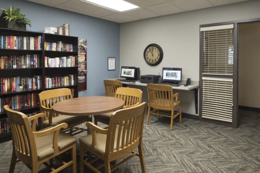 Library with circular table, a stocked bookshelf, and two desktop computers
