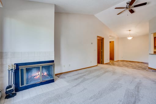 Empty living room with a corner fireplace, white carpets, and a ceiling fan