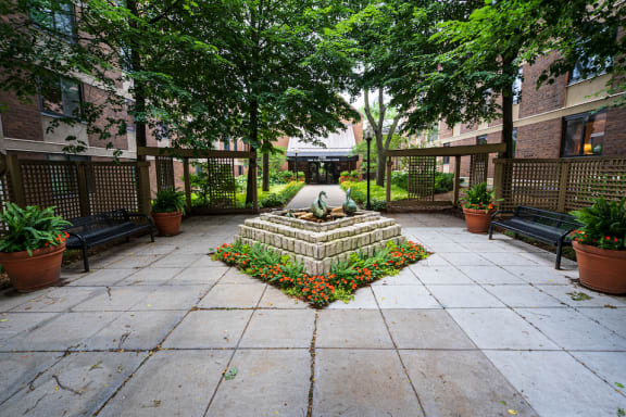 Enterance courtroom with stone centerpiece flanked by park benches and plants