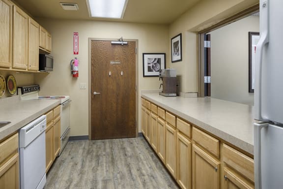Community kitchen with light wooden cupboards and a galley layout. A stove, oven, and microwave on the left, a refrigerator on the right