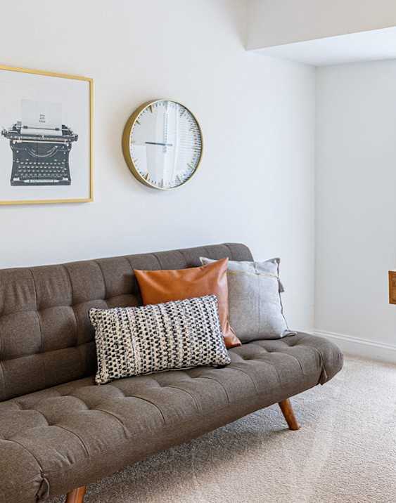 A grey couch with a green chair and a desk with a laptop and a plant on it.