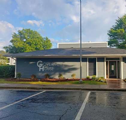a building with a sign on the side of a parking lot  at Governors House, Huntsville, AL, 35805