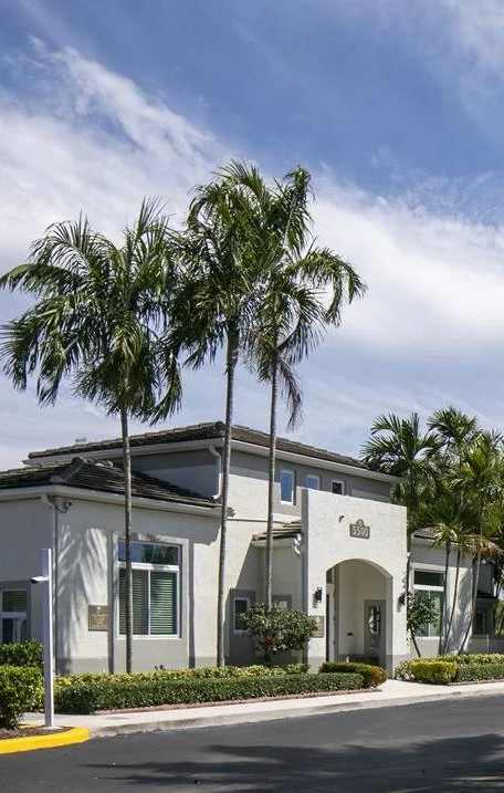 A building with a white facade is surrounded by palm trees.