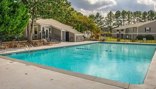 A large swimming pool surrounded by trees and a building in the background.