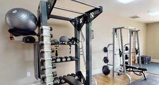 A home gym with a squat rack, dumbbells, and a bench.