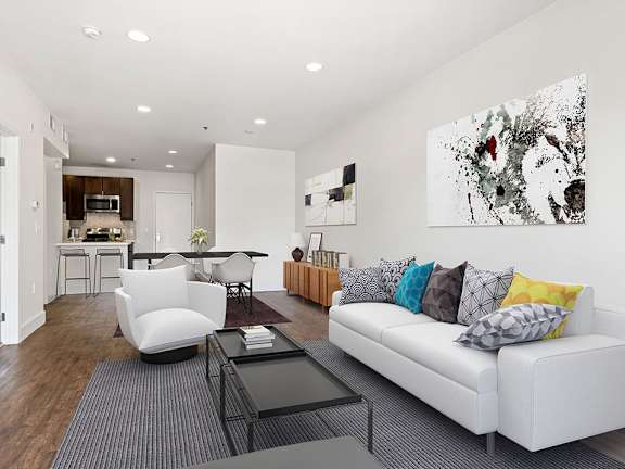 Hardwood floored living room with can lights and view of kitchen.