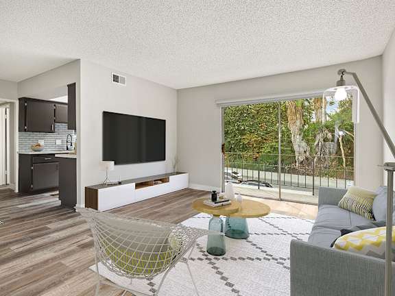 Hardwood floored living room with view of balcony and kitchen.