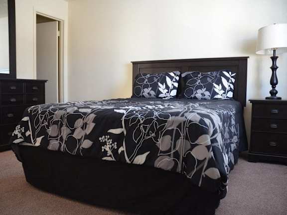 A bed with a floral patterned comforter and matching pillow cases sits in a bedroom with a lamp and nightstand.