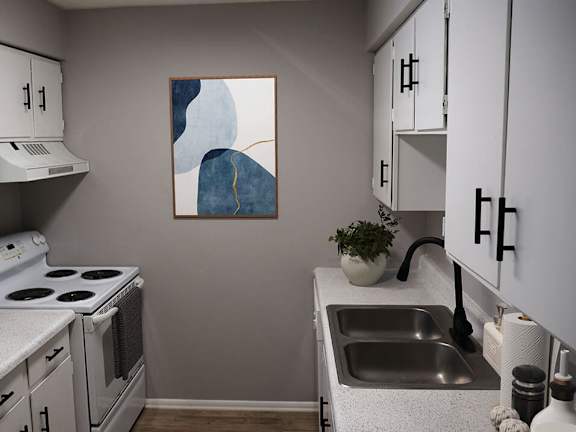 A kitchen with a white stove, white cabinets, and a painting on the wall.