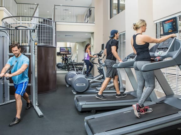 Four People Working Out in 24-Hour Fitness Center with Treadmills and Elliptical Machines at The Bartram Apartments in Gainesville, FL 32608