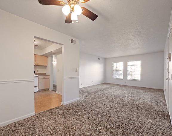 an empty living room with a ceiling fan and a kitchen
