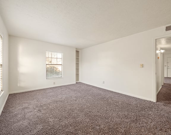 an empty living room with carpet and a door to a hallway
