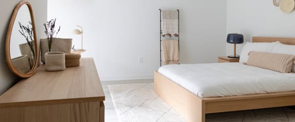 A bedroom with a bed, nightstand, and a wooden dresser with a mirror.