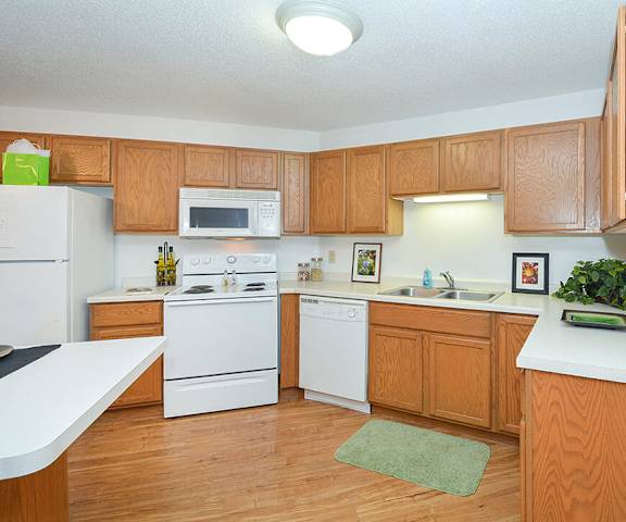 A large kitchen with white appliances, a light counter with lots of room, and spacious wooden cabinets at Quarry Commons Apartments. 