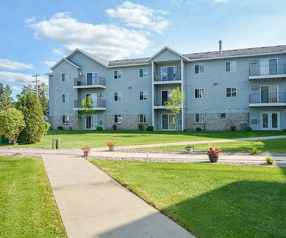 The pathway surrounded by grass and trees leading to the apartment building at Quarry Commons Apartments. 