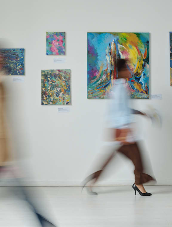 Person Walking Past Paintings in Art Gallery