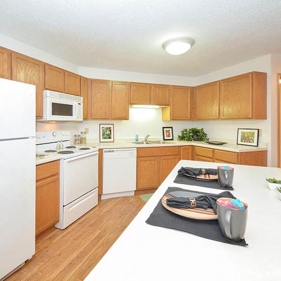 A large kitchen with white appliances, a light counter with lots of room, and spacious wooden cabinets at Quarry Commons Apartments. 