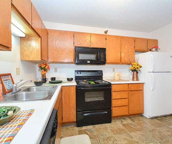 A large kitchen with black appliances, spacious marble countertops, and large wooden cabinets with decorations at Quarry Commons Apartments. 