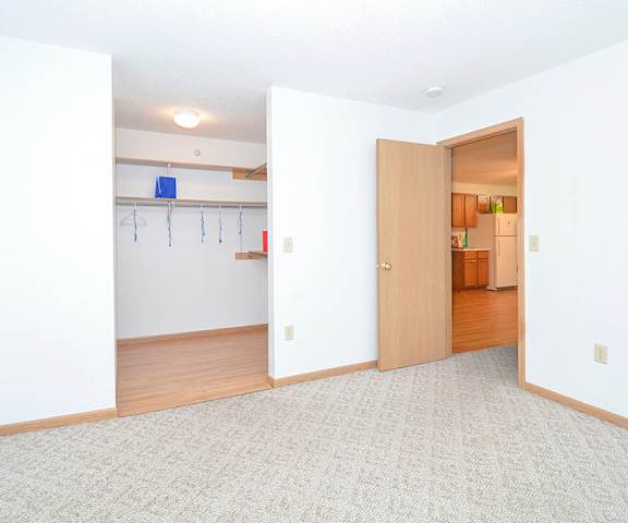 An empty carpeted bedroom with a large closet and white walls at Quarry Commons Apartments. 