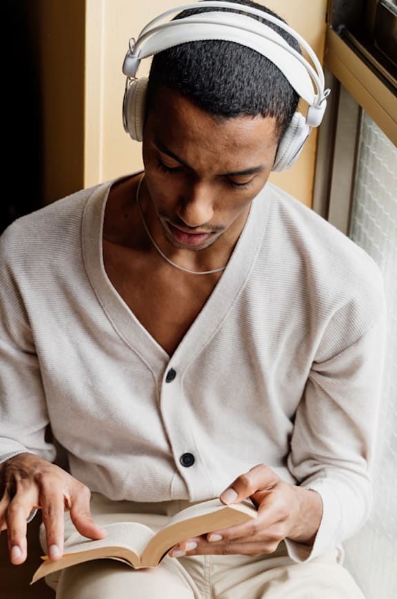 a man sitting on the floor wearing headphones and reading a book
