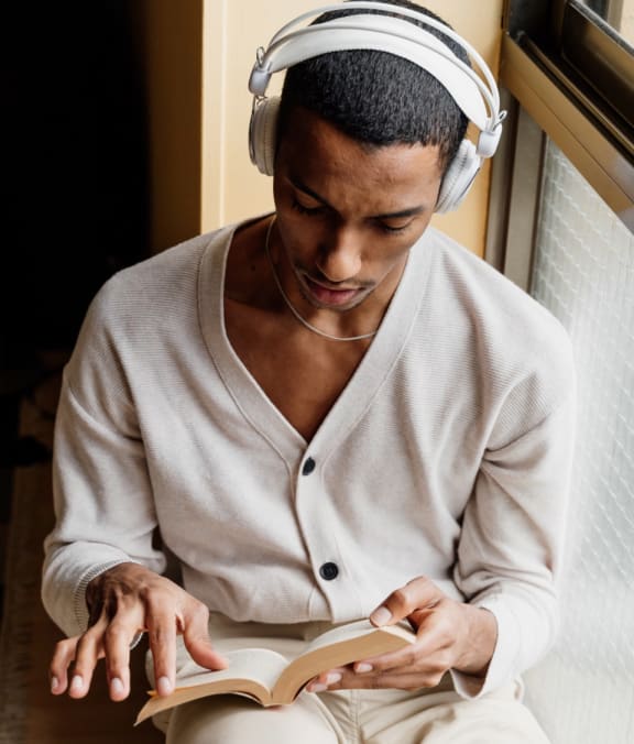 a man sitting on the floor wearing headphones and reading a book