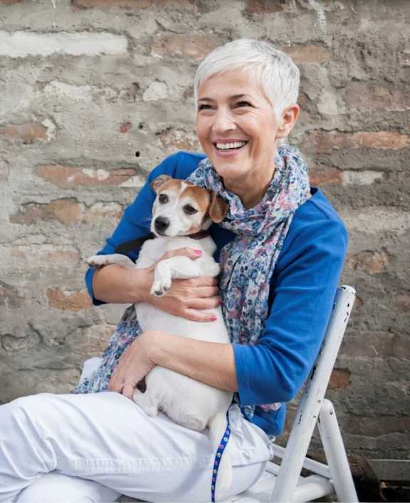 A woman with short hair is holding a small dog in her arms.