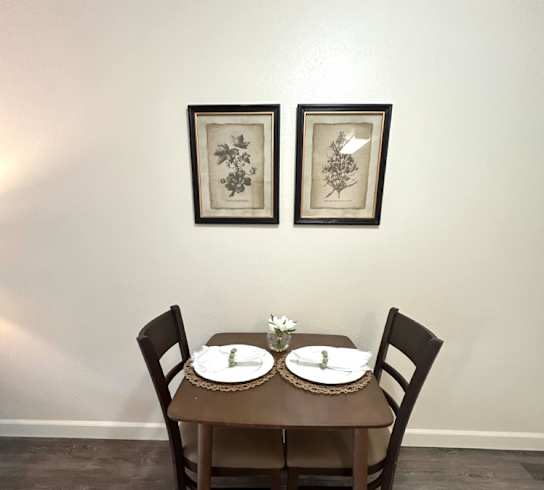 A brown table with two chairs and two pictures on the wall.