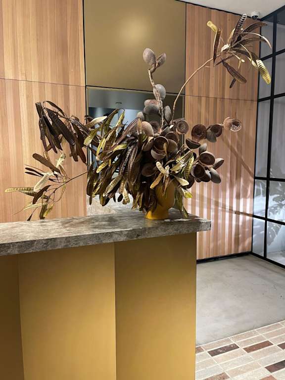 A large vase with dried flowers sits on a yellow counter.