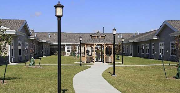A long black lamp post stands in front of a building with a green lawn in front of it.
