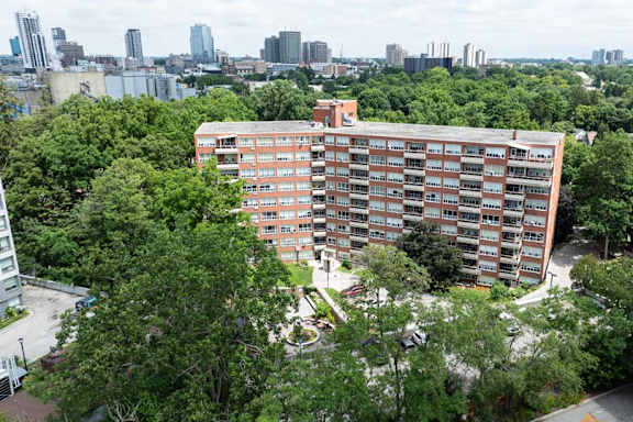 A large red building surrounded by trees with a city in the background.