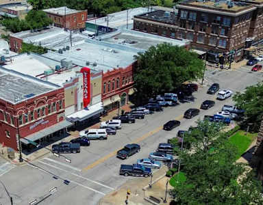A red brick building with a white roof is in the middle of a parking lot.