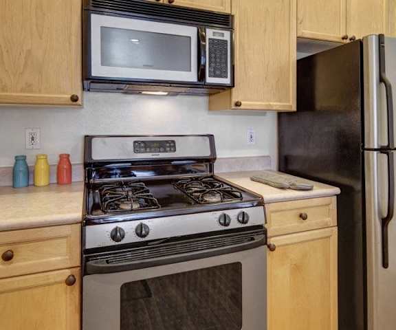 A cozy, modern kitchen with stainless steel appliances, kitchen utensils, light countertops with lots of room, and light, large wooden cabinets at the Highlands Luxury Residences. 