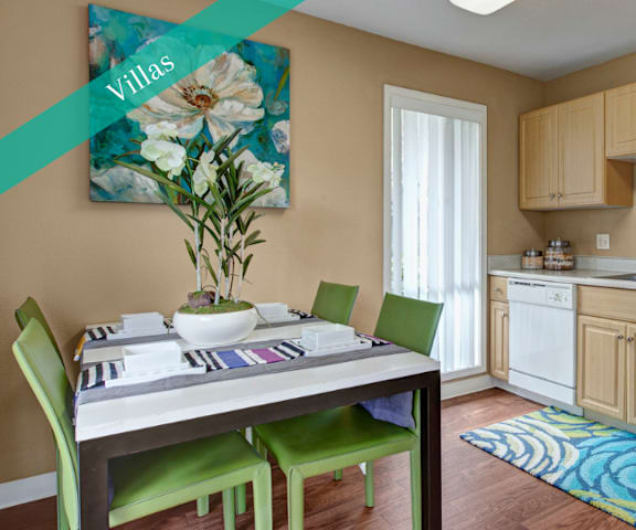 A kitchen with white appliances and counters, pale wood cabinets, and a table with green chairs at Capitol Towers - Towers and Villas