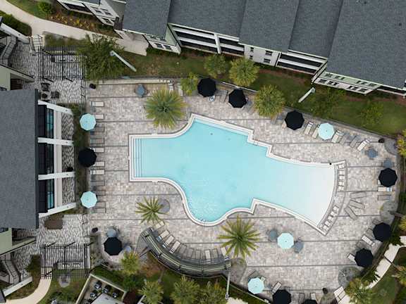 A large swimming pool surrounded by a stone patio and umbrella tables.