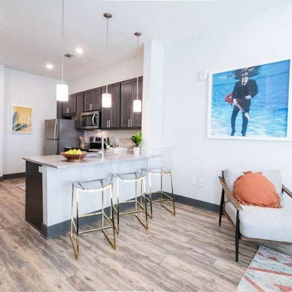 A kitchen with a bar and a chair with an orange pillow.