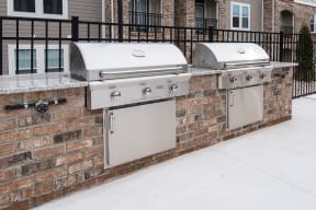 two stainless steel barbecue grills on a brick wall