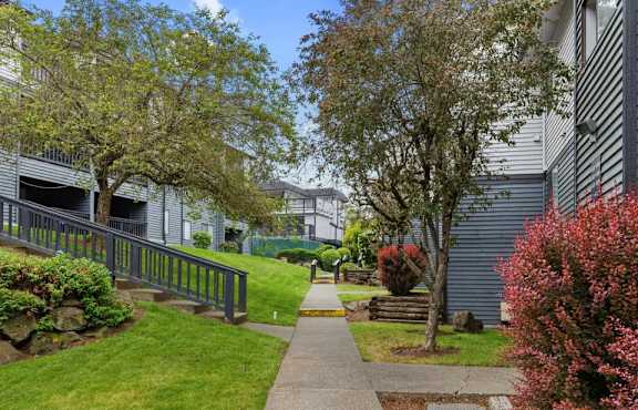 A residential area with a sidewalk, trees, and a building in the background.