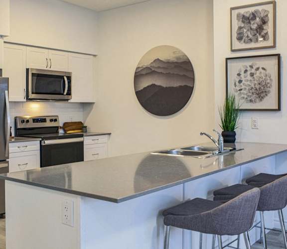 a kitchen with stainless steel appliances and a counter with three chairs