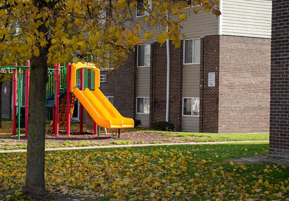A yellow slide in a playground surrounded by a tree with yellow leaves.