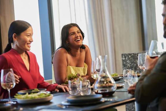 A group of people are sitting around a table with plates of food and glasses of wine.