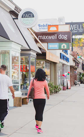 A man and a woman are walking down a street past a variety of shops.
